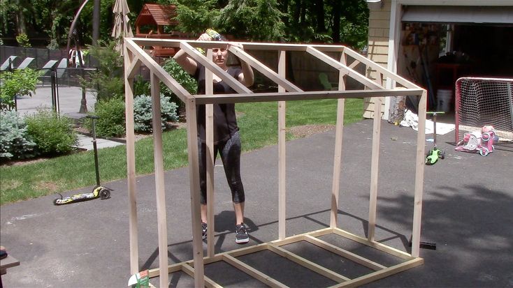 a woman standing in front of a house made out of plywood and some kind of wood