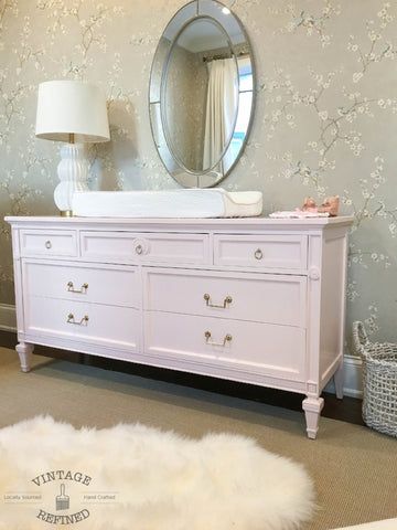 a white dresser sitting next to a mirror in a room with flowers on the wall