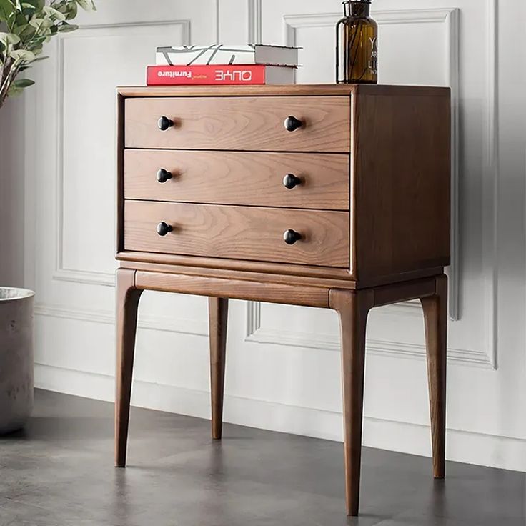 a wooden chest of drawers sitting on top of a floor next to a potted plant