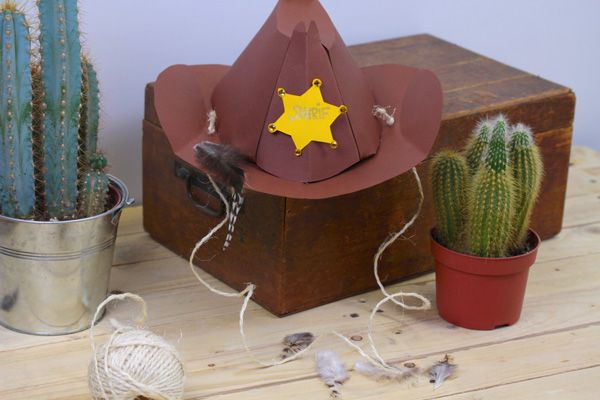 a toy cowboy hat sitting on top of a wooden box next to cacti