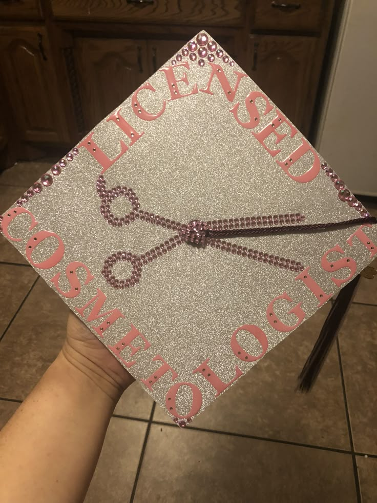 a person holding up a graduation cap with scissors on the front and writing across it