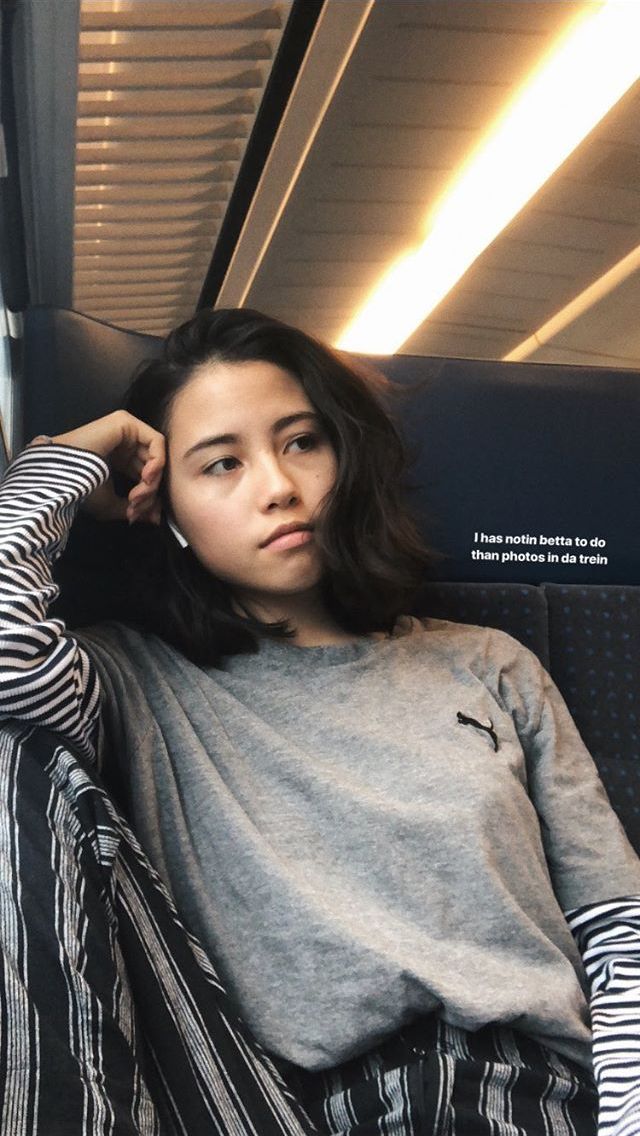 a young woman sitting on top of a train next to a window with her hand on her head