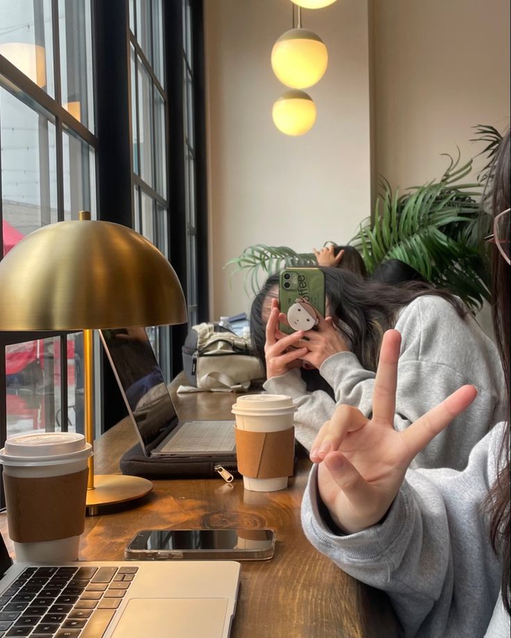 a woman taking a selfie with her cell phone at a table in front of a laptop