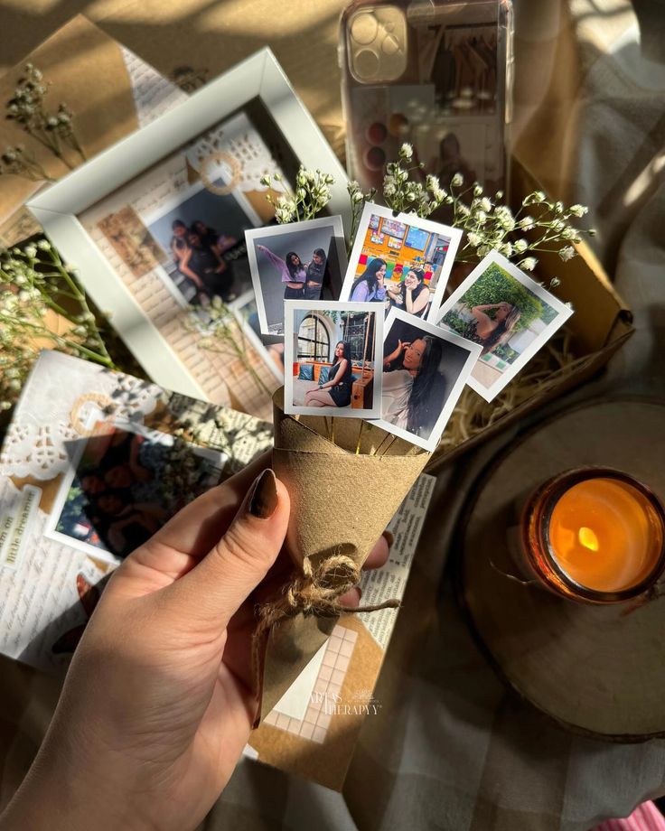 a person holding some pictures in their hand next to a candle and photos on the table