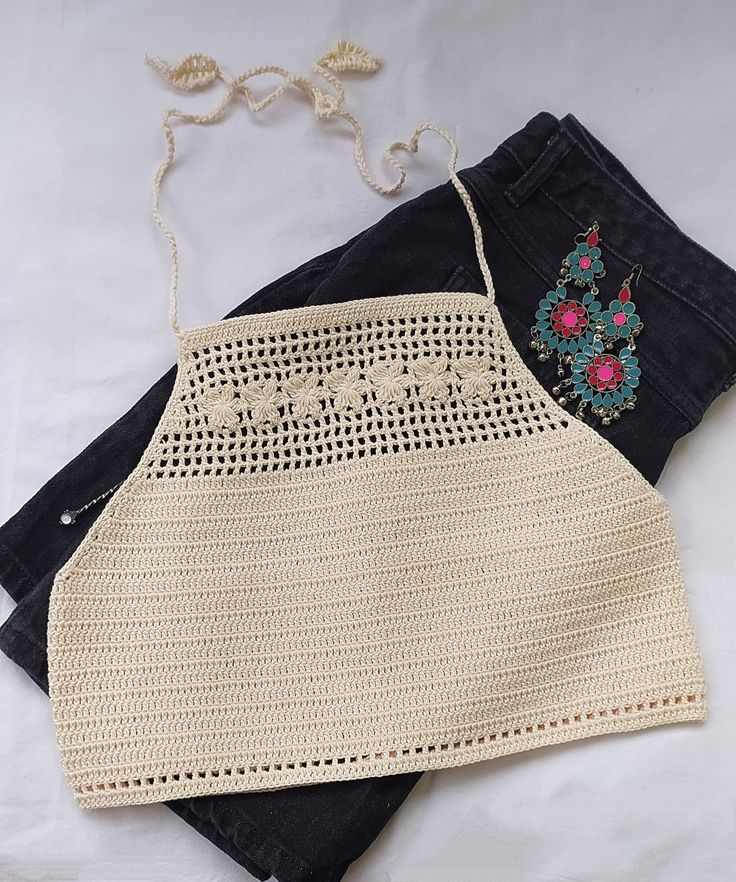 two crocheted aprons are sitting on top of each other next to jeans