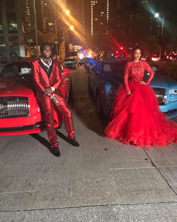 two people in red dresses standing next to some cars