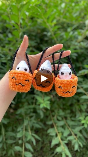 someone is holding up two small crocheted pumpkins with faces on their fingers