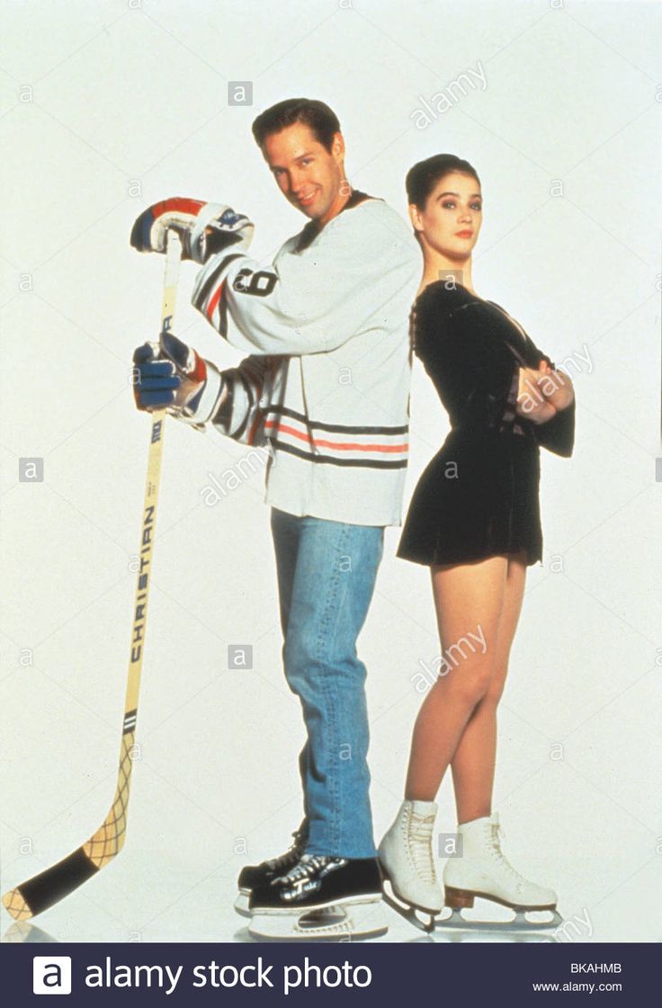 a man and woman standing next to each other in front of a white wall holding hockey sticks