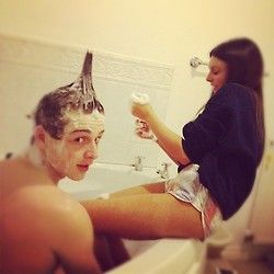 the man is shaving his hair in the bathroom while the woman looks at him