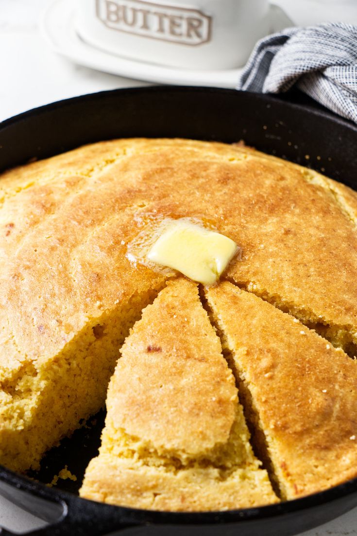 cornbread with butter in a cast iron skillet on a white tablecloth next to a cup