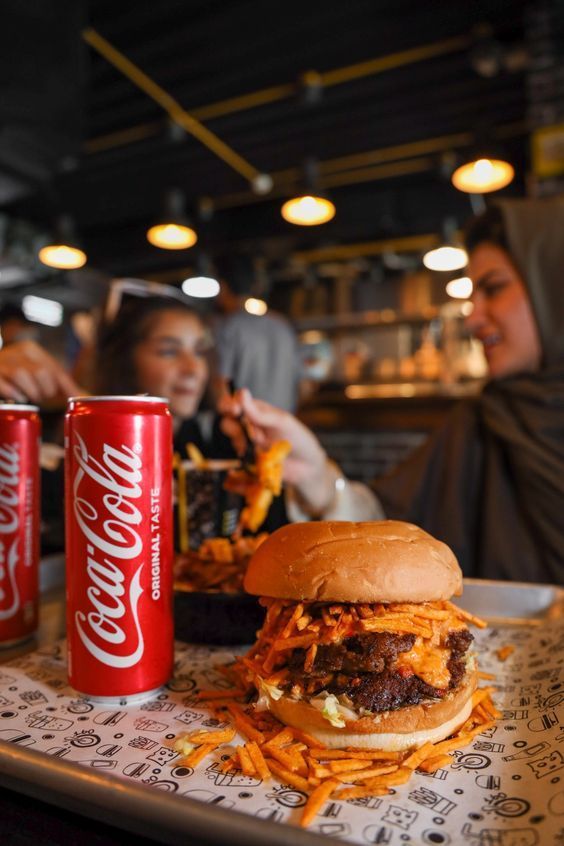 two women sitting at a table eating food and drinking coca colas in a restaurant