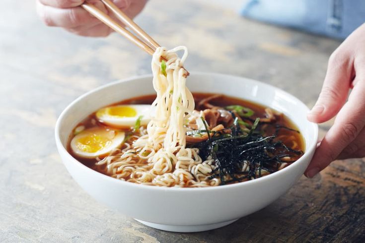 someone holding chopsticks over a bowl of ramen