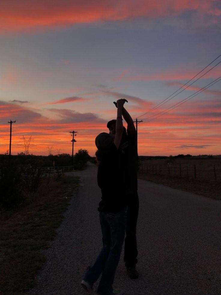 two men standing on the side of a road at sunset