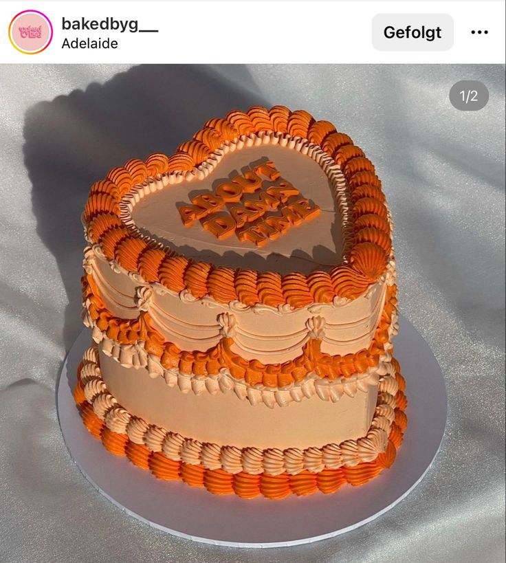 a heart shaped cake with orange icing on a white tableclothed surface, in the shape of a heart