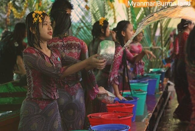 two women are washing their hands in buckets while others stand around and look on