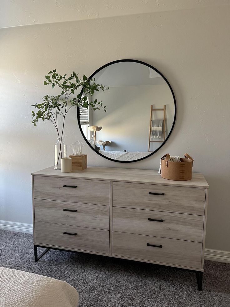 there is a mirror on the wall above a dresser with drawers and vases next to it