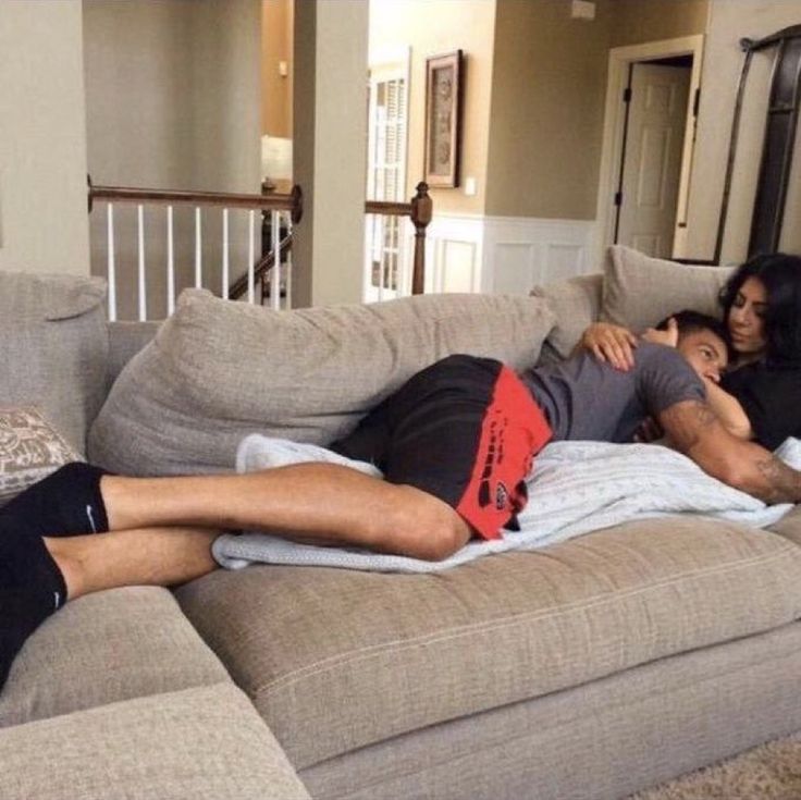 a man laying on top of a couch next to a woman with her arm around him