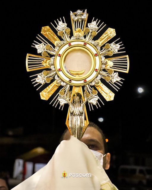 a man holding up a golden cross on top of a white cloth in front of his face