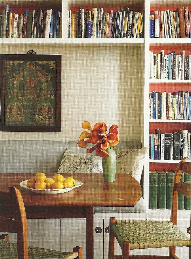 there is a bowl of fruit and flowers on the table in front of bookshelves