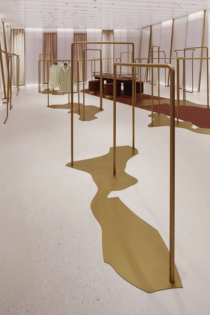 the interior of a store with gold colored metal racks and chairs on each side, along with white carpeted flooring