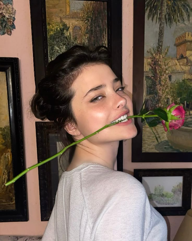 a woman holding a rose in front of her face and looking up at the camera