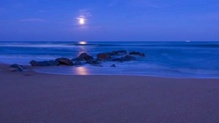 the moon is setting over the ocean and rocks