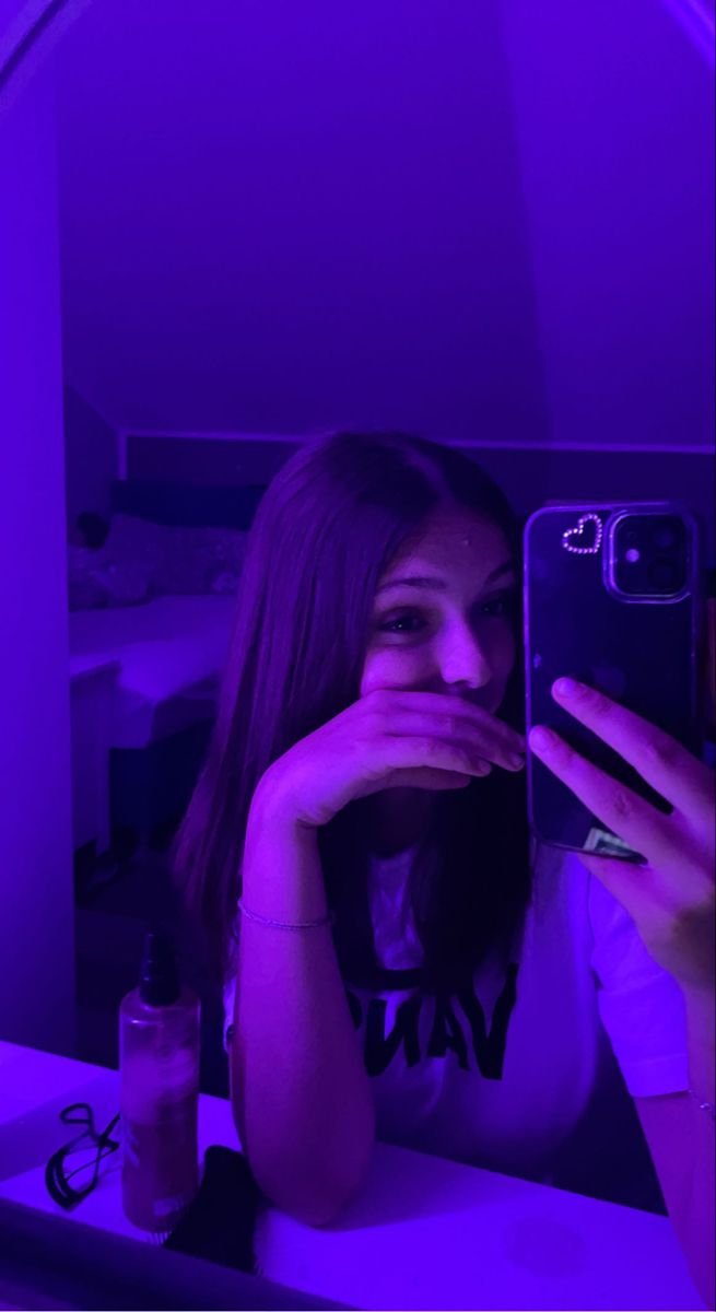 a woman taking a selfie with her cell phone in front of purple light at night