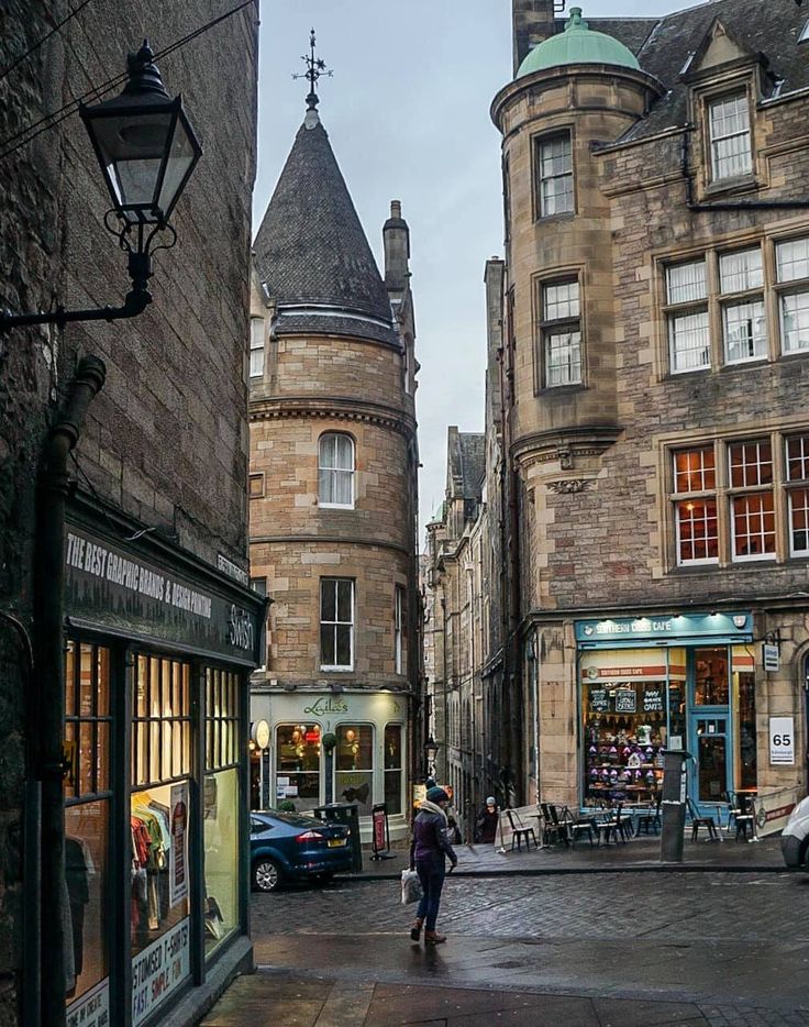 people are walking down the street in an old town with stone buildings and tall towers