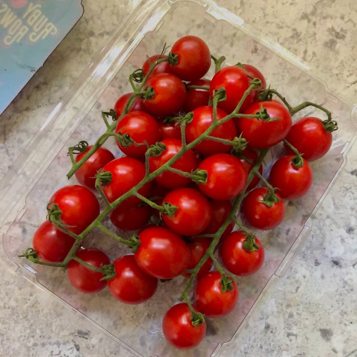 a plastic container filled with red tomatoes on top of a marble countertop next to a book