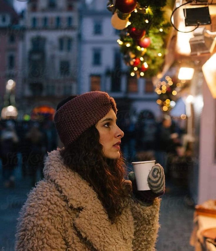 a woman in a fur coat is holding a coffee cup and looking at the street