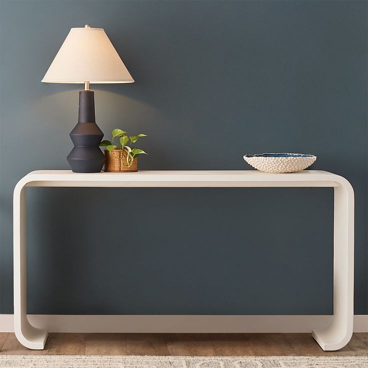 a table with a lamp on it next to a vase and bowl in the corner