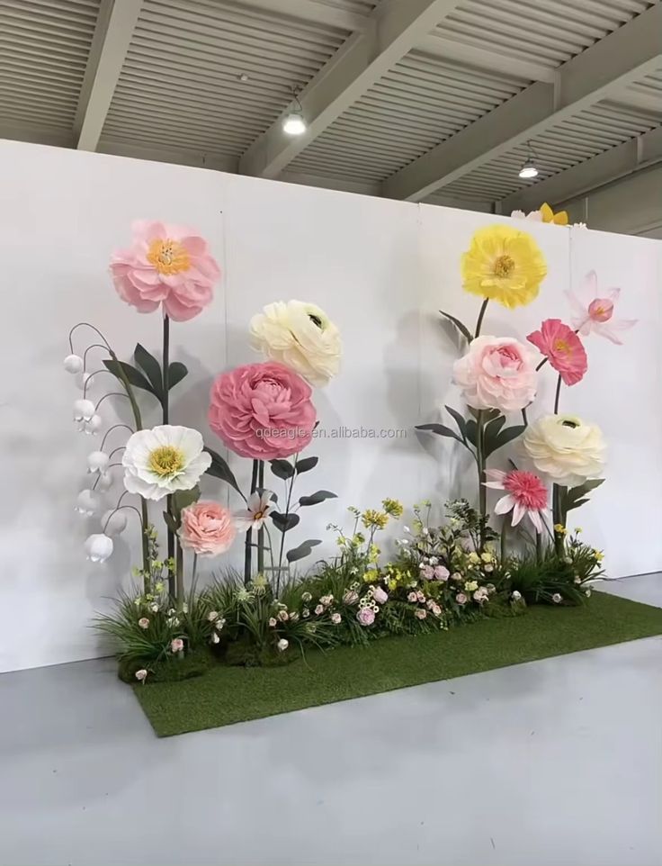 an artificial flower display is displayed in front of a white wall with flowers on it