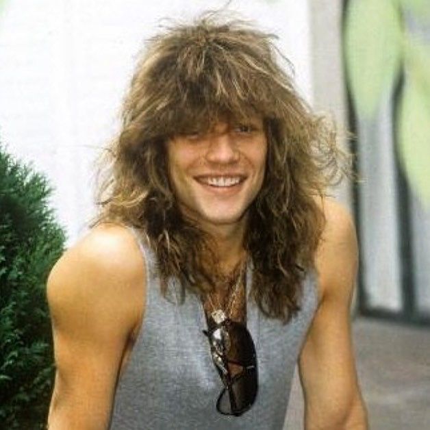 a young man with long hair is smiling for the camera while holding a skateboard