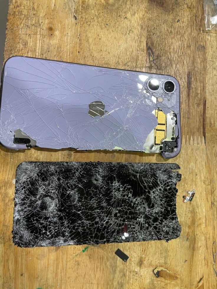 an iphone that has been smashed and is sitting on a table next to another broken phone