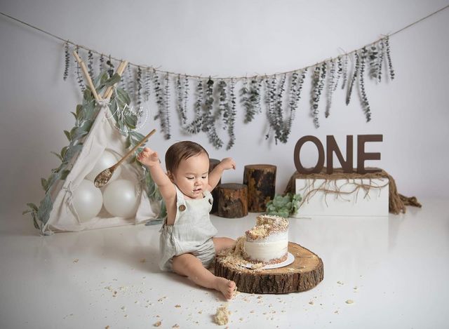 a baby sitting on the floor with a cake in front of it and decorations behind him