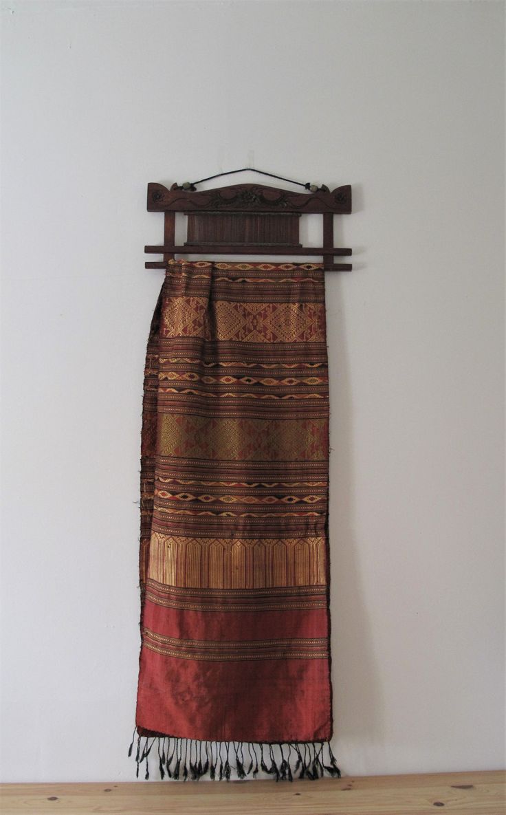 a wall hanging on the side of a white wall next to a wooden rack with a brown and red blanket