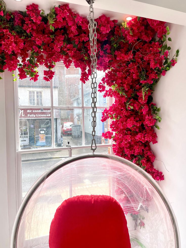 a red chair sitting in front of a window with flowers on the wall behind it