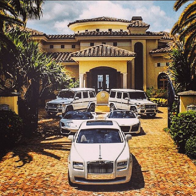 a group of cars parked in front of a large yellow building with palm trees on the driveway