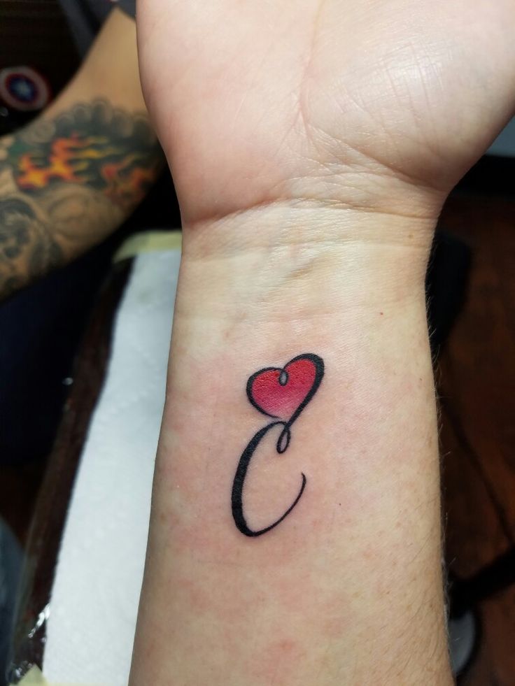 a person with a tattoo on their wrist holding up a red heart and the letter c