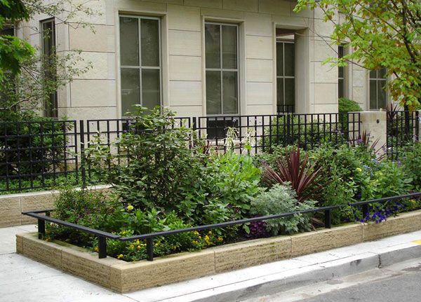 a planter filled with lots of plants next to a building on the side of a street