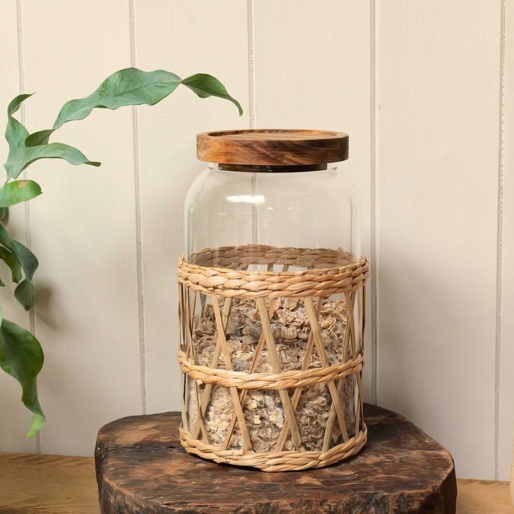 a glass jar filled with dried nuts sitting on top of a wooden table next to a potted plant