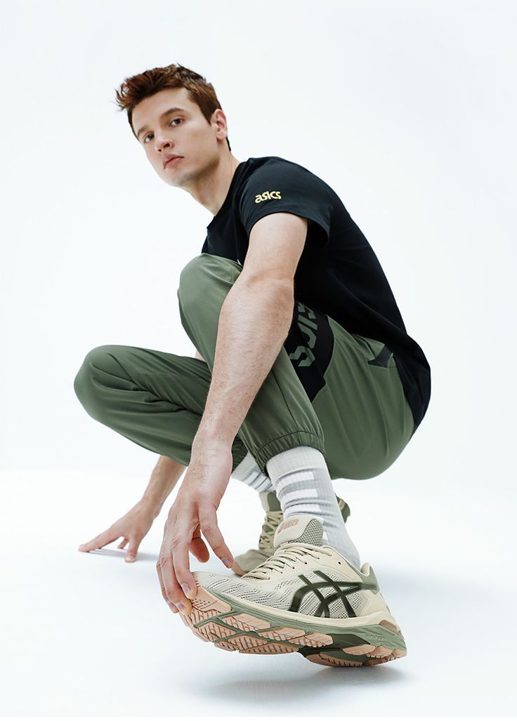 a man squatting on one leg with his hands in the air while wearing sneakers