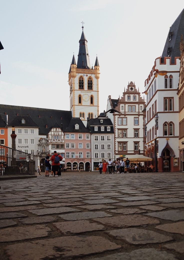 people are walking around in an old european town with cobblestone streets and tall buildings