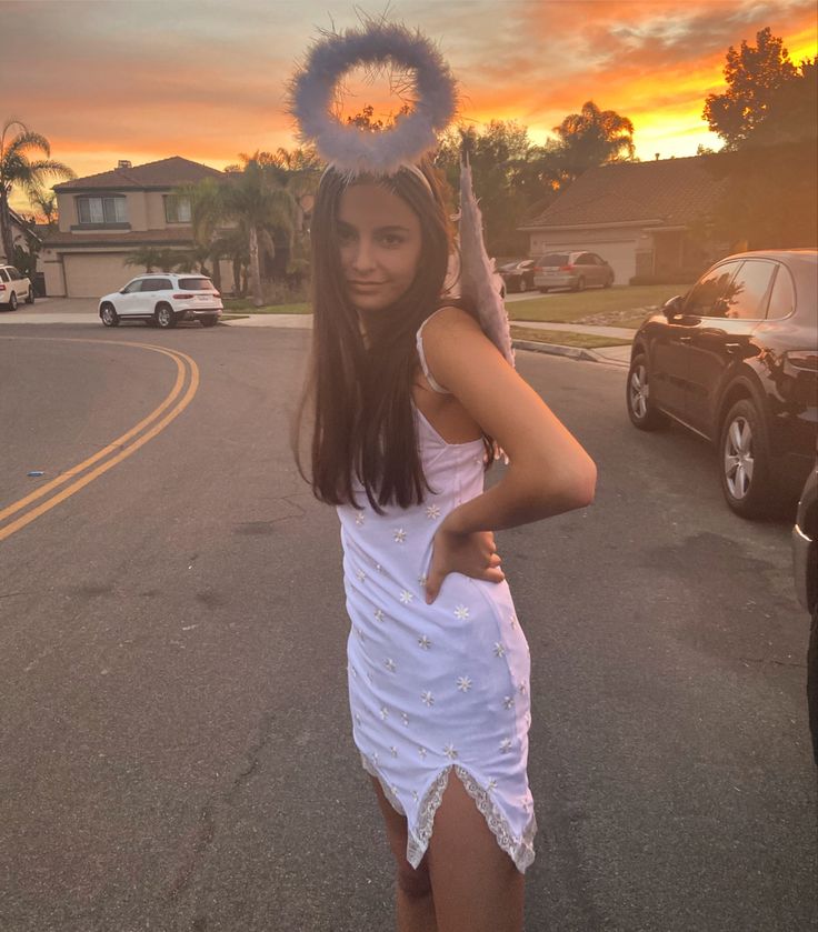 a woman in a white dress is standing on the street with her hands behind her head