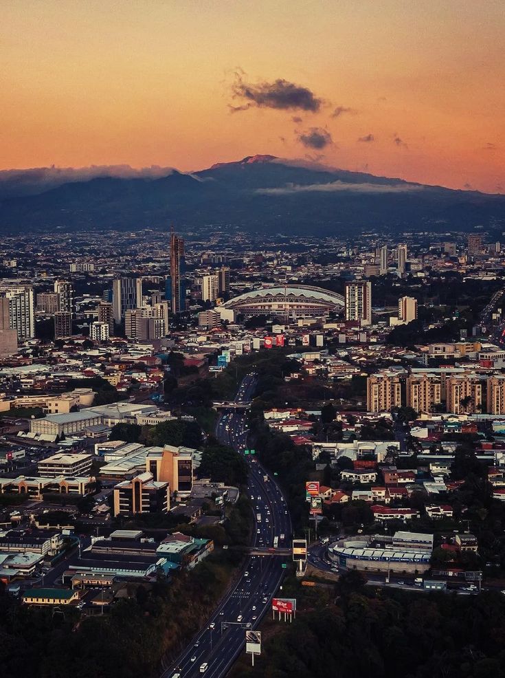 an aerial view of a city at sunset with mountains in the distance and cars on the road