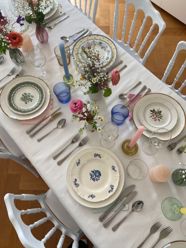 the table is set with plates, silverware and flowers in vases on it