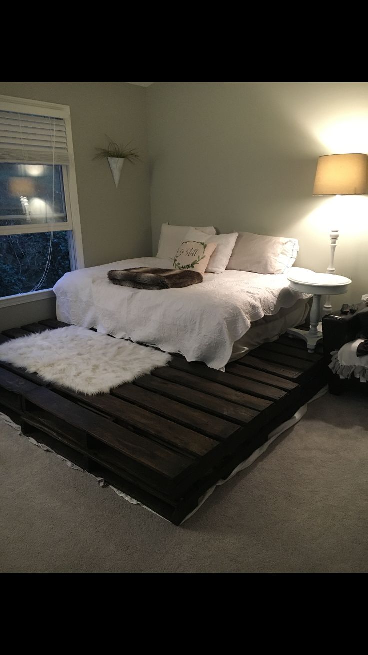 a bed made out of pallet wood with white sheets and pillows on it, next to a window