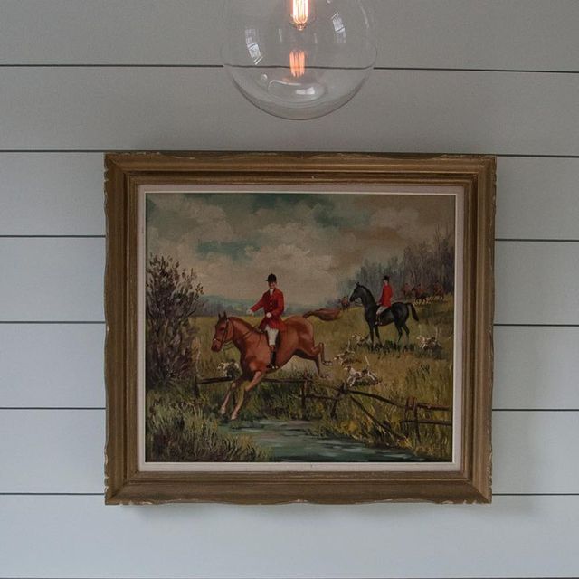 a painting hanging on the wall next to a light fixture with a horse and rider in it