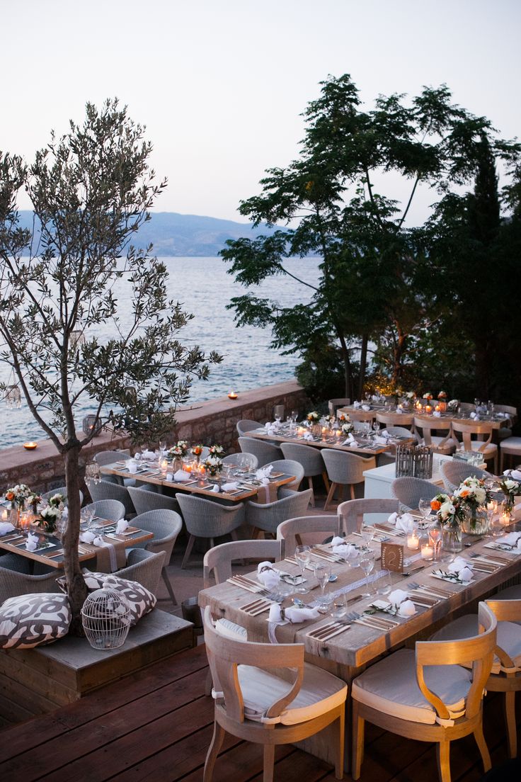 an outdoor dining area overlooking the water with tables and chairs covered in white linens