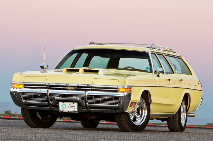 an old yellow station wagon is parked on the side of the road near the ocean